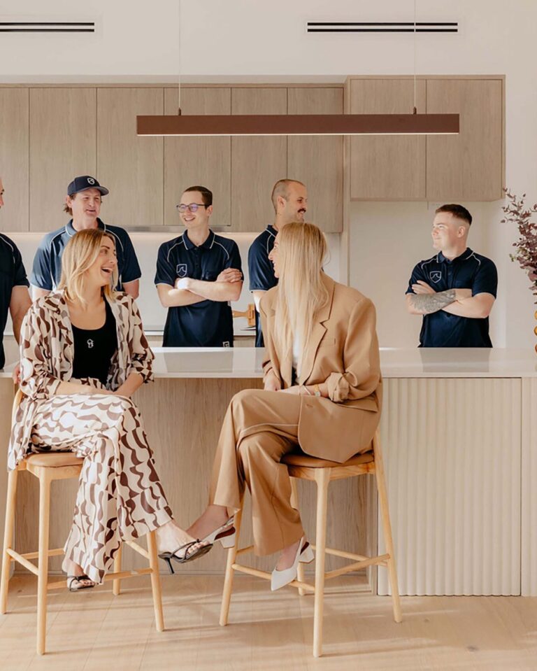 Indianic Homes team gathered in contemporary kitchen with timber cabinetry and curved island bench