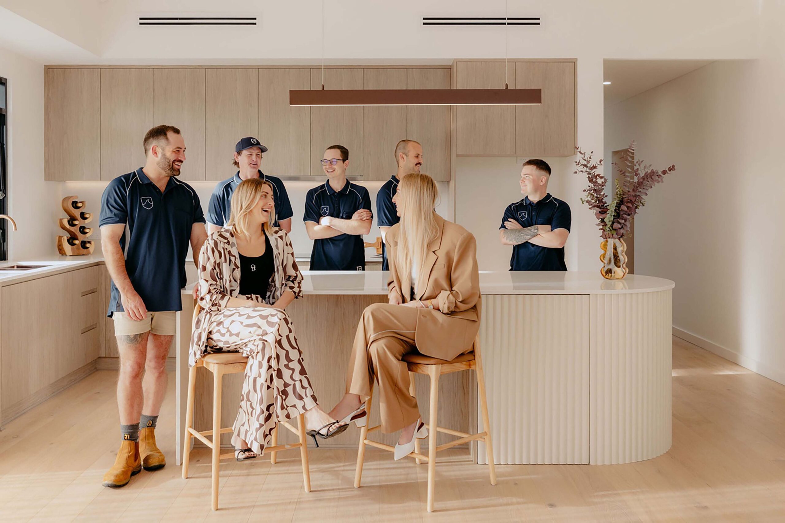 image2 Indianic Homes team gathered in contemporary kitchen with timber cabinetry and curved island bench