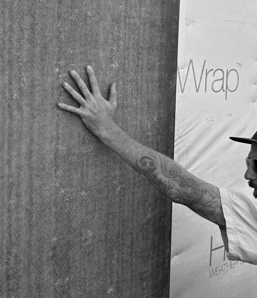 Hands-on quality control on an Indianic Homes build site Builder with tattooed arm pressing hand against weatherboard cladding panel on a construction site in South West Western Australia