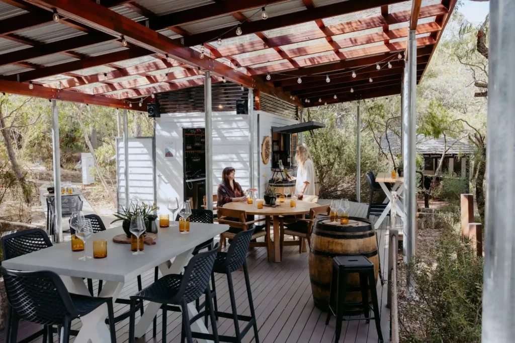 Two guests enjoying a wine tasting experience at Valle du Venom cellar door in Yallingup, seated on the covered deck surrounded by native bushland